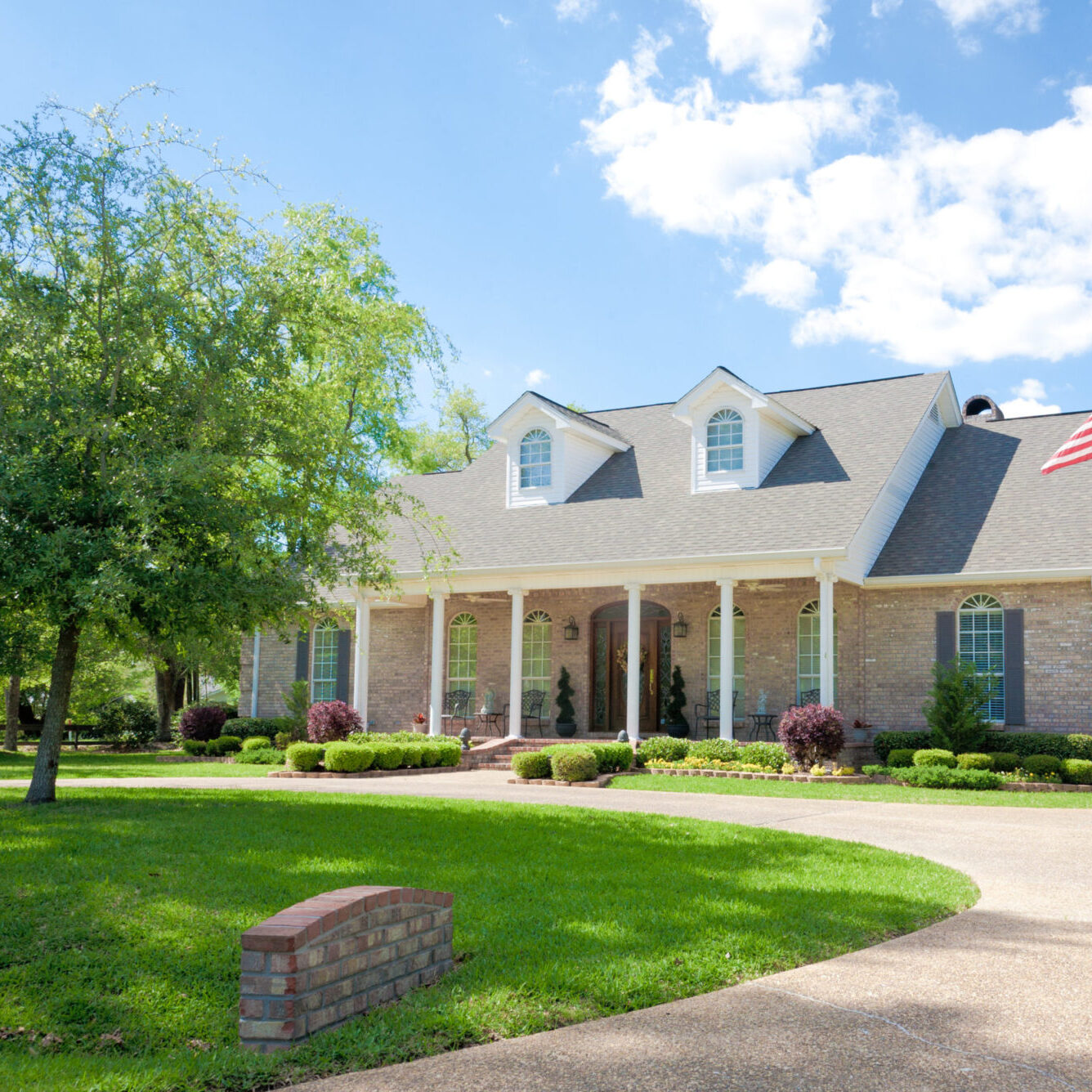 Large ranch style coastal home with a front porch. The yard features a grass lawn trees. A driveway leads to the home.