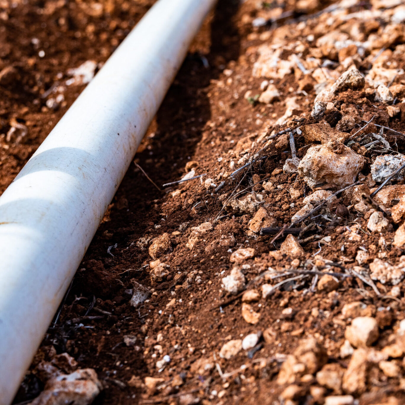 PVC pipe in dirt trench outdoors for plumbing water drainage installation. Underground irrigation system.